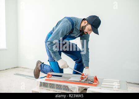 Workman cutting ceramic tiles with handy machine at the construction site indoors Stock Photo