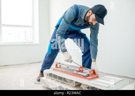 Workman cutting ceramic tiles with handy machine at the construction site indoors Stock Photo