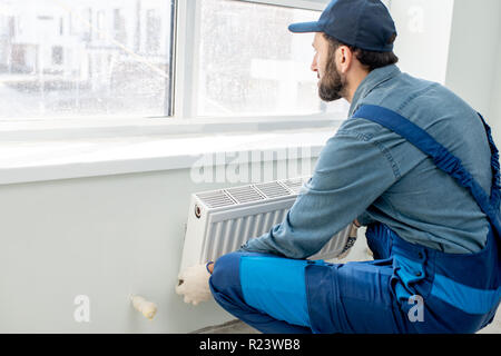 Workman mounting water heating radiator near the window in the white renovated living room Stock Photo
