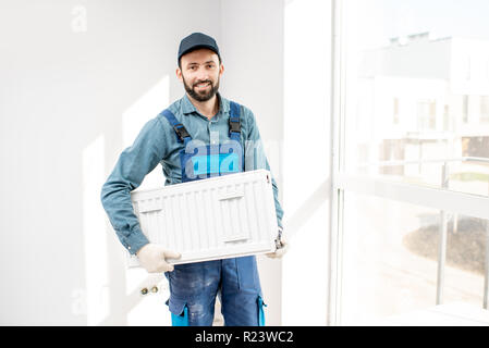 Portrait of a workman holding heating radiator in the white room Stock Photo