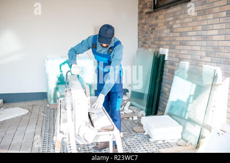 Builder in uniform cutting tiles with big electro saw on the construction site outdoors Stock Photo