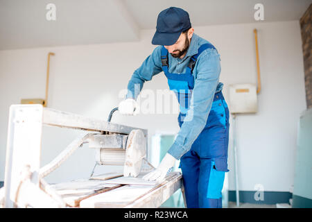 Builder in uniform cutting tiles with big electro saw on the construction site outdoors Stock Photo