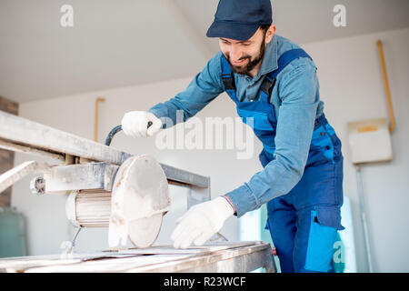 Builder in uniform cutting tiles with big electro saw on the construction site outdoors Stock Photo