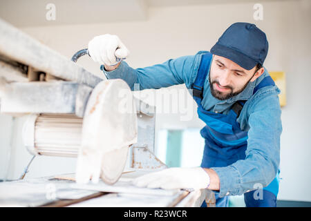 Builder in uniform cutting tiles with big electro saw on the construction site outdoors Stock Photo