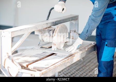 Builder in uniform cutting tiles with big electro saw on the construction site outdoors Stock Photo