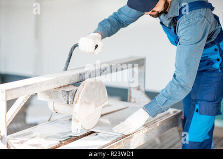 Builder in uniform cutting tiles with big electro saw on the construction site outdoors Stock Photo