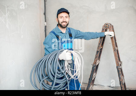 Portrait of a handsome electrician in uniform with electric cable indoors Stock Photo