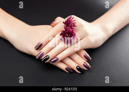 Black and burgundy manicure with flowers on black background. Gel nail polish with mirror powder pigment. Body care Stock Photo