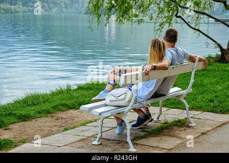 Beautiful scenery with young couple sitting on the bench near the Bled Lake, Slovenia Stock Photo