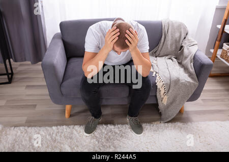 Young Man Sitting On Sofa Suffering From Headache Stock Photo
