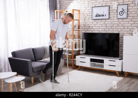 Disabled Young Man Using Crutches To Walk On Carpet Stock Photo