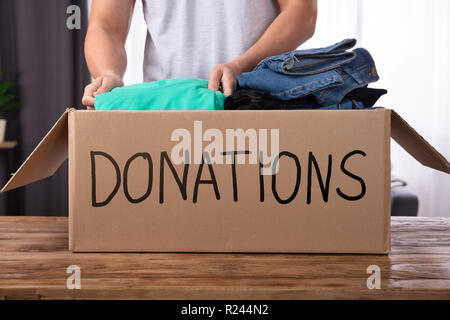 Young Man Donating Clothes In Donation Box Over Wooden Desk Stock Photo