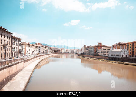 Horizontal photo with river Arno which goes through famous town Pisa in Italy Tuscany. Water is brown. Buildings are on both sides. Hills are in backg Stock Photo