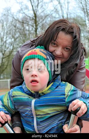 Defect,childcare,medicine and people concept- happy mother and son with down syndrome playing in a playground. Stock Photo