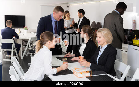 Cheerful multinational work team having break at office, drinking coffee and talking Stock Photo