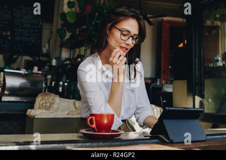 businesswoman having a video chat on digital tablet while sitting at coffee shop. Female sitting at window table at cafe and making video call using e Stock Photo