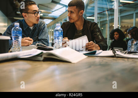 Two young students studies together on an assignment. Classmates sitting together at tablet with books and discussing. Stock Photo