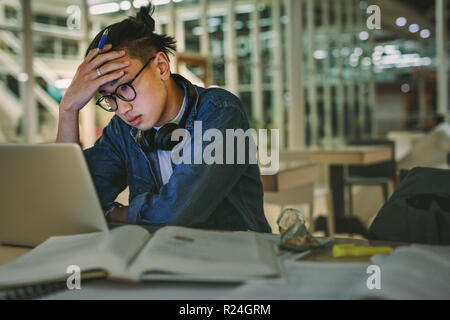 Male student sitting at library looking at laptop with hand on forehead. Depressed student sitting in library with laptop in college. Stock Photo