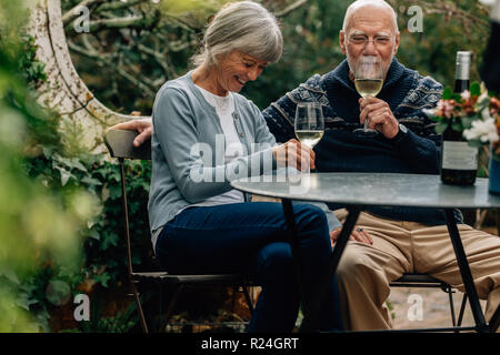 Happy senior couple drinking wine sitting at a table in their backyard. Old woman sitting with her husband drinking wine and talking. Stock Photo
