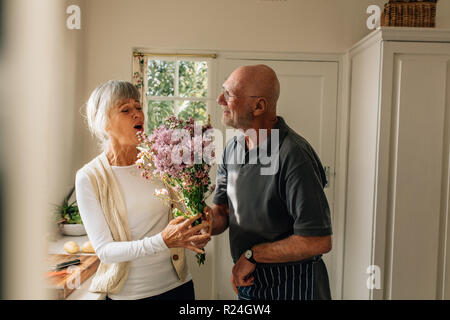 Man expressing his love for his wife giving her a bunch of flowers at home. Senior woman happy to see her husband give her a bouquet of flowers. Stock Photo