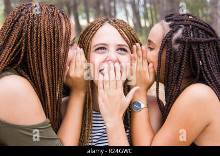 Three young and beautiful girls, with braided hair, laughing and whispering secrets Stock Photo