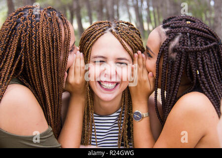 Three young and beautiful girls, with braided hair, laughing and whispering secrets Stock Photo