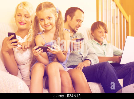 Happy mom, dad and two kids working with smartphones indoors Stock Photo