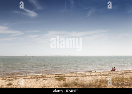 landscape images taken from a walk around the island of east mersea in essex england with two people sitting on the beach looking out to sea Stock Photo