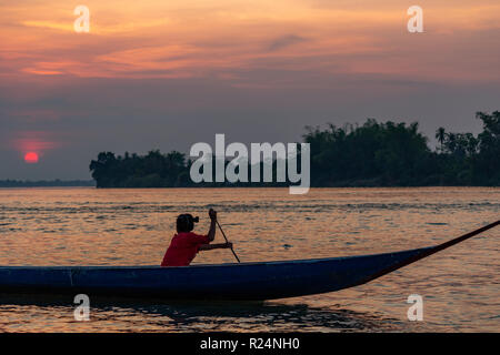 Don Det, Laos - April 22, 2018: Girl rowing a wooden boat over the Mekong river at sunset  near the Cambodian border Stock Photo