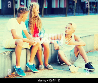 Happy adult kids spending time together outdoors discussing and using phones Stock Photo