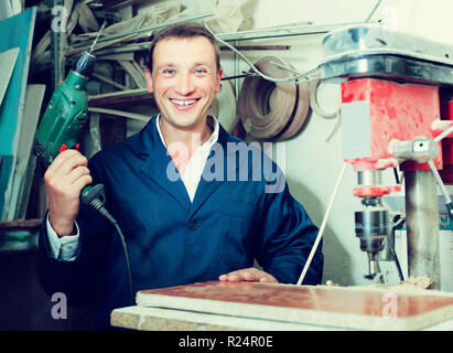 portrait of happy man in uniform working with electrical screwdriver on plywood indoors Stock Photo