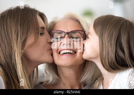 Grown daughter and granddaughter kissing happy old grandmother o Stock Photo