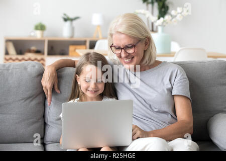 Smiling grandma and cute kid granddaughter watching cartoons on  Stock Photo