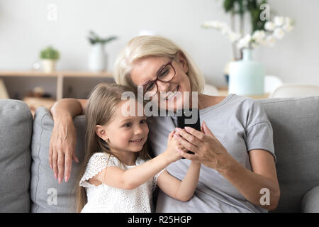 Happy grandmother and cute granddaughter using cellphone making  Stock Photo
