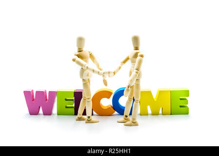 Wooden figures posing as business men shaking hands in front of the word WELCOME, high key isolated on white. Stock Photo