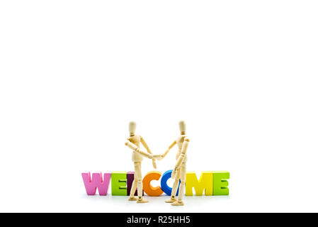 Wooden figures posing as business men shaking hands in front of the word WELCOME, high key isolated on white and copy space on the top Stock Photo