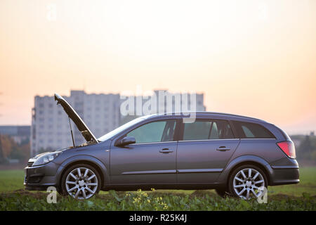 Side view of empty silver car with open hood on empty gravel field road on clear bright sky copy space background. Transportation, vehicles problems a Stock Photo