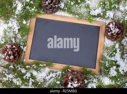 Blank chalkboard for copy space bordered with snow covered pine cones and evergreen tree branches Stock Photo