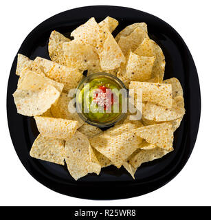 Top view of spicy corn tortilla chips nachos with guacamole on black plate. Isolated over white background Stock Photo
