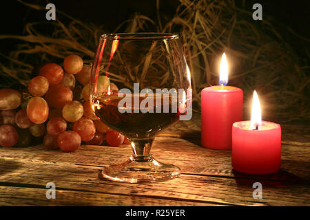 christmas candles, grapes and glass with cognac or whisky on wood background. Christmas decoration. Stock Photo