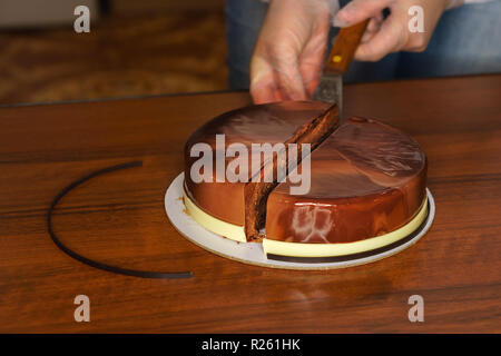 Prague mousse cake. Woman cuts off piece of cake with a kitchen knife. Mirror glaze glitters deliciously. Modern cooking. Cooking in a pastry shop. Stock Photo