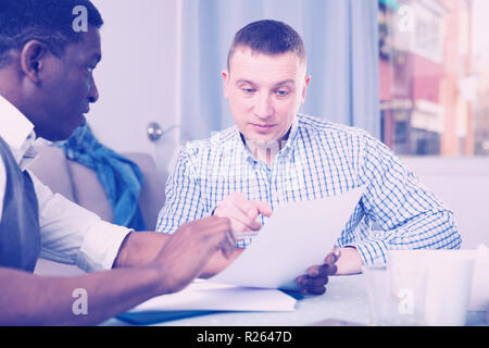 Portrait of two men in serious discussion at home table while analysing documents together Stock Photo