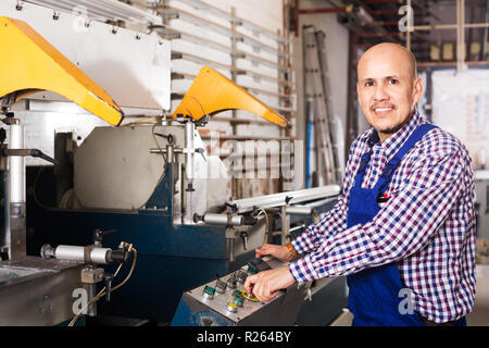 Positive workman in uniform working on lathe machine at factory Stock Photo