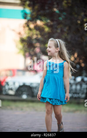 High angle of adorable cheerful little girl in blue dress with toy on hand  having fun on paved walkway in summer day stock photo - OFFSET