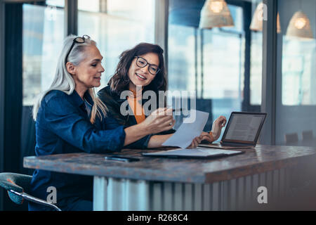 Two women analyzing documents while sitting on a table in office. Woman executives at work in office discussing some paperwork. Stock Photo