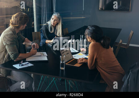 Three professionals sitting around a table and discussing work. business team brainstorming new business ideas during meeting at office. Stock Photo
