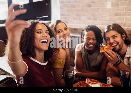 Group of happy multiracial friends taking selfie on a smart phone while having party at pizza restaurant. Excited friends taking selfie with phone whi Stock Photo