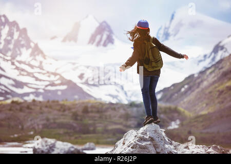 Girl stands on big rock and looks at snow capped mountains. Travel, backpacker or tourism concept Stock Photo