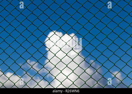 clouds against a blue sky against a metal grid of green, closeup in a fenced area Stock Photo