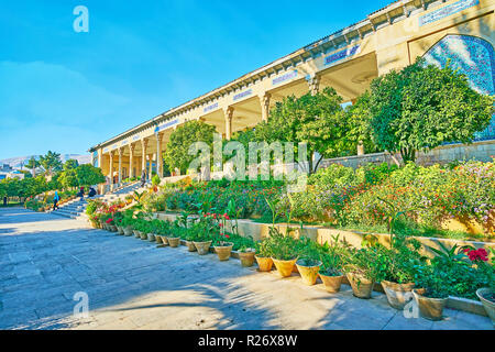 The beautiful flower beds and colored flowers in pots decorate the entrance to Mussala Gardens with long colonnade and covered gallery in Persian styl Stock Photo